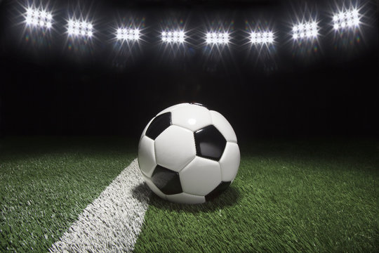 Traditional soccer ball on grass field under lights at night