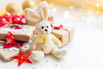 Christmas and New Year background with toy plush rabbit, presents and decorations for Christmas tree. Holiday background with stars confetti and light bulbs. Place for text.
