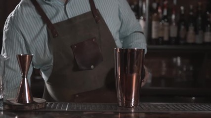 Bartender is making cocktail at bar counter, adding some bitter in the shaker