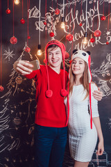 Happy couplein funny hats standing hugging and make selfie on a dark background with Christmas pattern. New year.