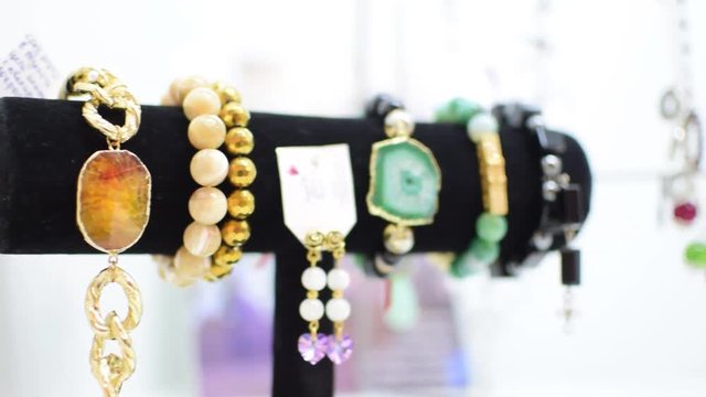 jewelry green black white yellow purple necklace and bracelet and earrings closeup on black hangers on white shelf or on a white table. In the background is an interior designer.