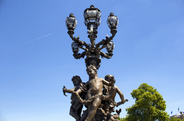 Historical street lamp made with 3 children statues on Pont Alexandre III in Paris. Ornate, late 19th-century arched bridge in a Beaux Arts style & named after a Russian czar