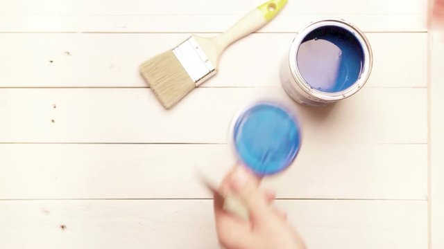 A can of blue industrial paint is being opened by an artist