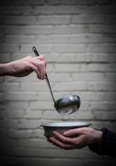 Homeless. In the hands of one man metal plate. In the hand of another person ladle.
