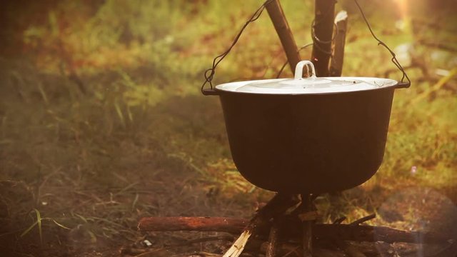Campfire scene: a pot with food hangs over the fire