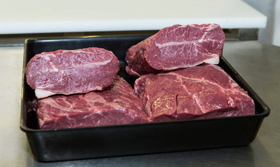 Several pieces of raw beef back of the black bowl on the table, ready for cutting on the BBQ.