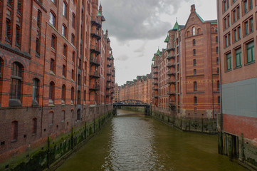 Fototapeta na wymiar HAMBURG, GERMANY - JULY 18, 2015: the canal of Historic Speicherstadt houses and bridges at evening with amaising skyview over warehouses, famous place Elbe river.