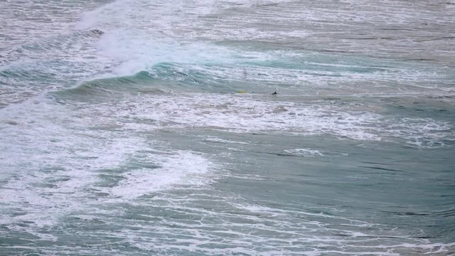 A lone swimmer struggling large sea waves. Dramatic aerial seascape view with man and force of nature in 4k Ultra HD 3840x2160
