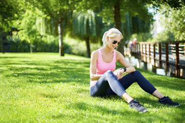 Starting morning outdoor. Full length shot of a fit woman sitting in the grass and checking her sport watch after morning workout.