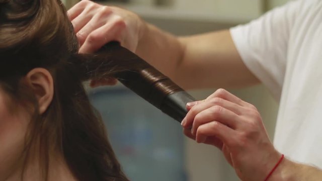 Hairdresser makes hair styling by using curling in a beauty salon for woman