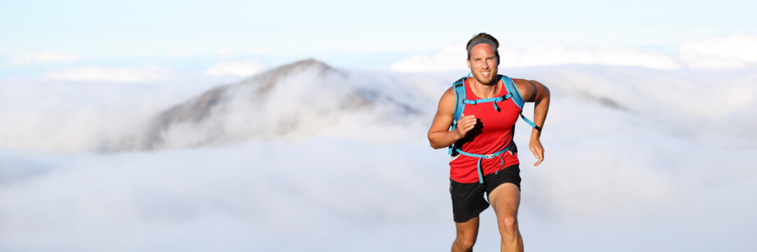 Trail runner man athlete running in mountains outdoor nature with mountain peak in clouds in background. Panorama horizontal banner landscape crop for copyspace.