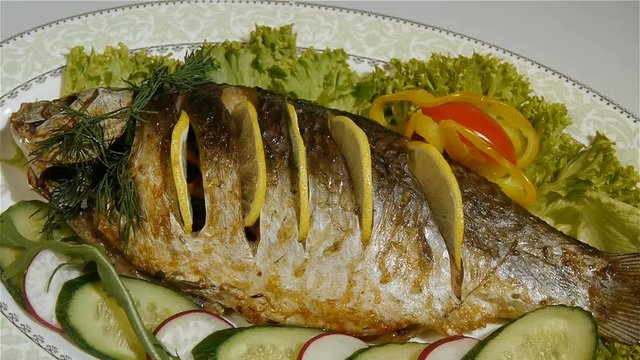 Baked carp with spices and lemon on white pan top view