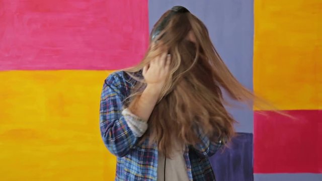 Woman listening to music, dancing and closing face by long hair. Colorful background