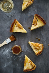 Pieces of pear almond cream tart with glass of white wine and jam. Flat lay. Dark grey background. Food photography