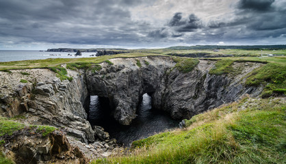 Dungeon national Park, Newfoundland featuring a rare natural occurrence of rock formation under which, two tunnels comprise a haunting face - earning it its local nickname, Devil's eyes. - 129120423