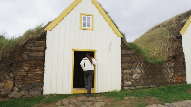 Iceland tourist by Old Farmhouse Laufas Glaumbaer farm Folk Museum turf roof houses in Varmahlid, Skagafjordur. Icelandic tourist destination and attraction landmark. Woman walking Icelandic sweater.