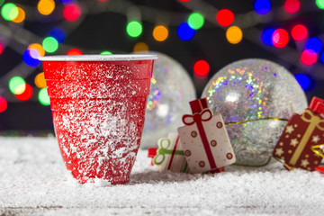 bicchiere di plastica nella neve, con addobbi natalizi e luci sullo sfondo