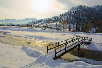 A bridge over a small creek, winter in the village, the ground u