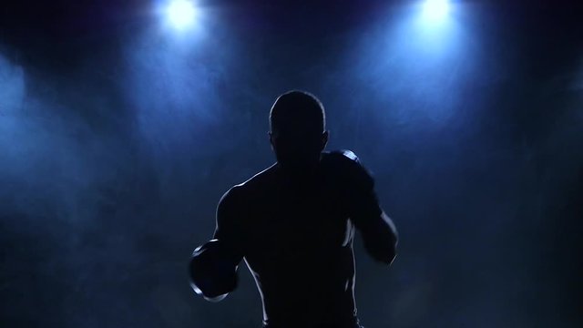 Boxer fulfills blows facing the viewer in slow motion. Silhouette