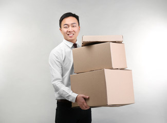 Handsome Asian man with cardboard boxes on light background