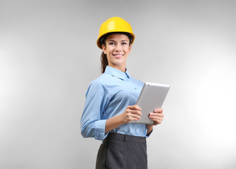 Confident young woman with hardhat and tablet computer, on light background