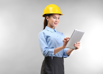 Confident young woman with hardhat and tablet computer, on light background