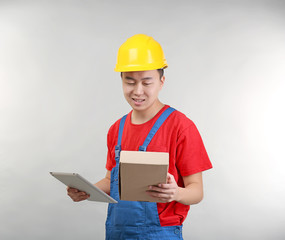 Asian warehouse worker with tablet computer and cardboard box, on light background