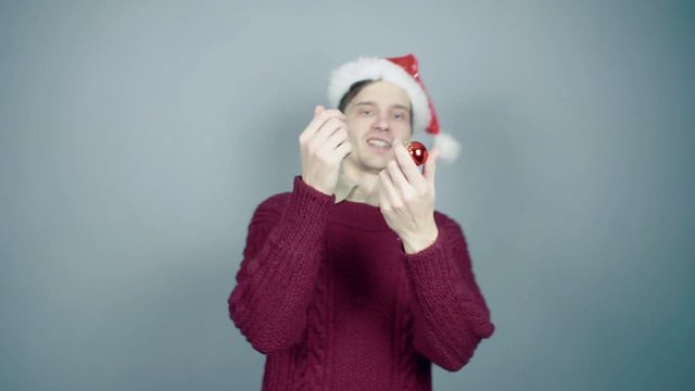 Young man in santa hat unsuccessfully juggles with Christmas decorations