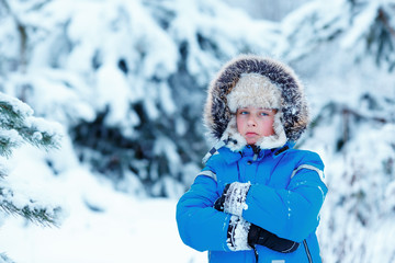 Cute little boy wearing warm clothes playing on winter forest