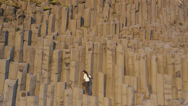 Iceland woman tourist walking on basalt columns on Reynisfjara black sand beach of Vik, South Iceland coast. Happy woman visiting tourist attraction destination. RED EPIC SLOW MOTION