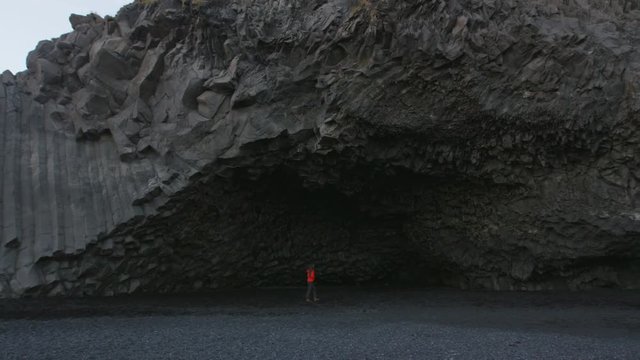 Iceland tourist woman walking on Reynisfjara black sand beach by basalt columns and cave, beach of Vik, South Iceland coast. Happy woman visiting tourist attraction destination. RED EPIC SLOW MOTION