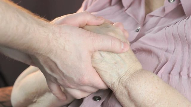 Man holding the old wrinkled hands of elderly woman. Man soothes the elderly woman during stress. Close up