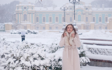 Winter portrait of a woman in white coat during snowfall in a park