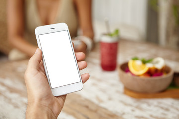 People, technology and communication concept. Cropped shot of man messaging online, checking newsfeed on his mobile phone, using free wireless internet connection, relaxing at cafe with his wife
