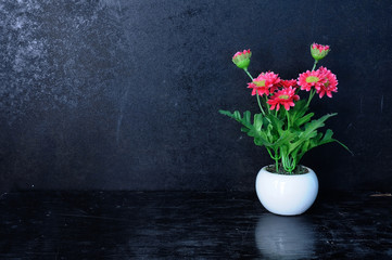 Small pot with artificial flowers on black background.