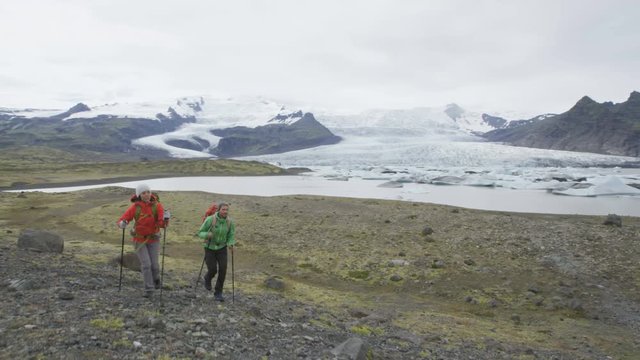 Adventure hiking trekking travel people on Iceland. Hikers walking by glacier and glacial lagoon / lake of Fjallsarlon  Vatnajokull National Park. Couple visiting Icelandic nature. RED EPIC.