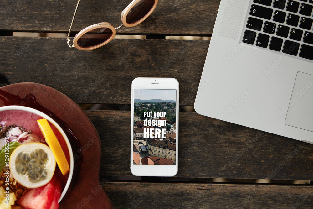 Poster top view of mobile phone with copy space screen for your design resting on wooden table with laptop,