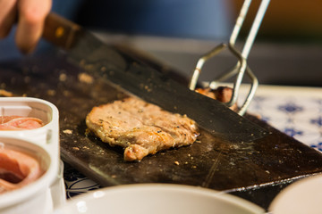 Hand cutting a slice of pork meat on chopping wood.