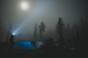 A man with lantern at night is tent in misty forest