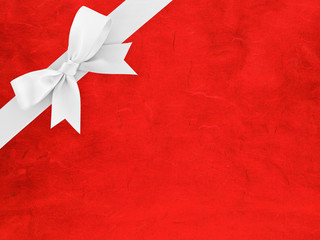 white ribbon bow wrapped around corner of bright red paper with abstract striped pattern, simple...