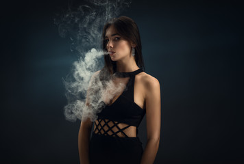 Sexy girl in a black dress smoking electronic cigarette