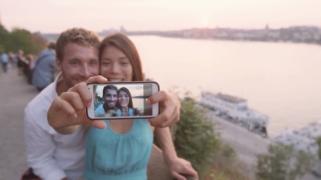 Couple taking selfie self portrait in Stockholm. Candid fresh Scandinavian man and Asian woman looking at old town cityscape sunset view from Monteliusvagen overlooking Gamla Stan  the old city.