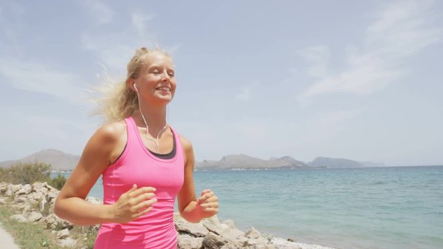Jogging woman running woman outside on beach. Female fitness runner girl jogger training listening to music in earphones. Beautiful young blonde woman in her 20s. RED EPIC Footage in REAL TIME.