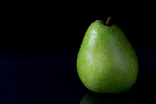 Low key picture of green pear with drops of water on a black background.