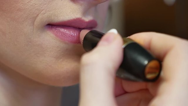 Girl paints her lips face and skin with lipstick indoor