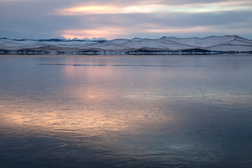 Winter landscape with lake covered with thin layer of colorful ice, sunset, in soft colors