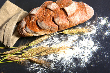rustic crusty bread and wheat ears on a dark wooden table