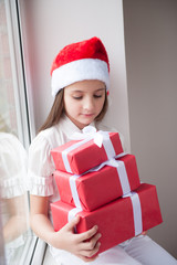 beautiful girl in Santa hat sitting at window and keeps gifts