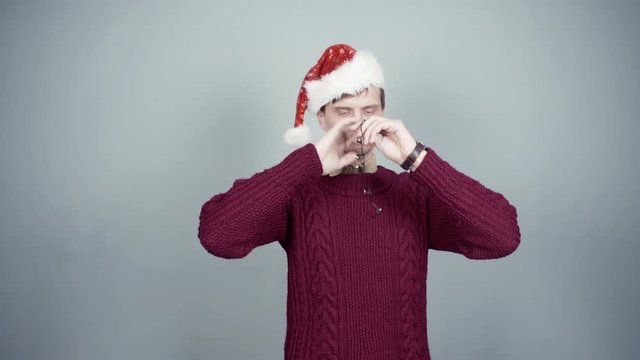 Young man in knitted sweater and santa hat entangled in flashing garland Christmas preparation