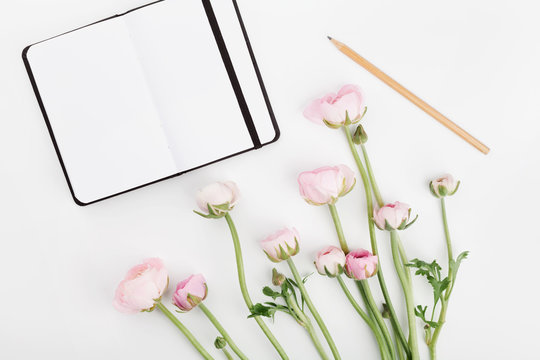 Beautiful spring Ranunculus flowers and empty notebook on white desk from above. Mockup. Pastel color. Clean space for text. Flat lay style.